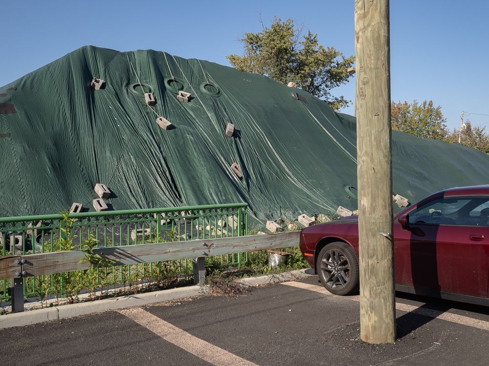 a pile of something covered in a huge green tarp held down by ropes and cinder blocks